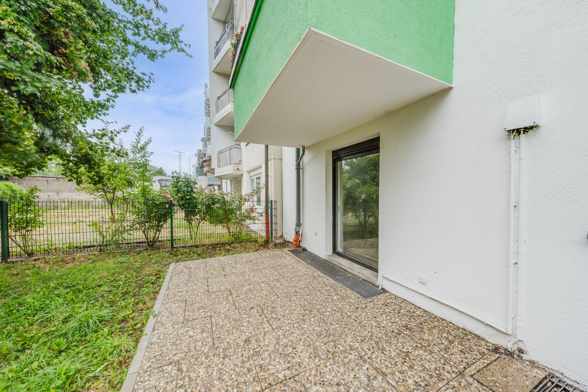 Terrasse mit Steinboden und Glastür, angrenzend an einen kleinen Garten, im Erdgeschoss eines Wohnhauses.