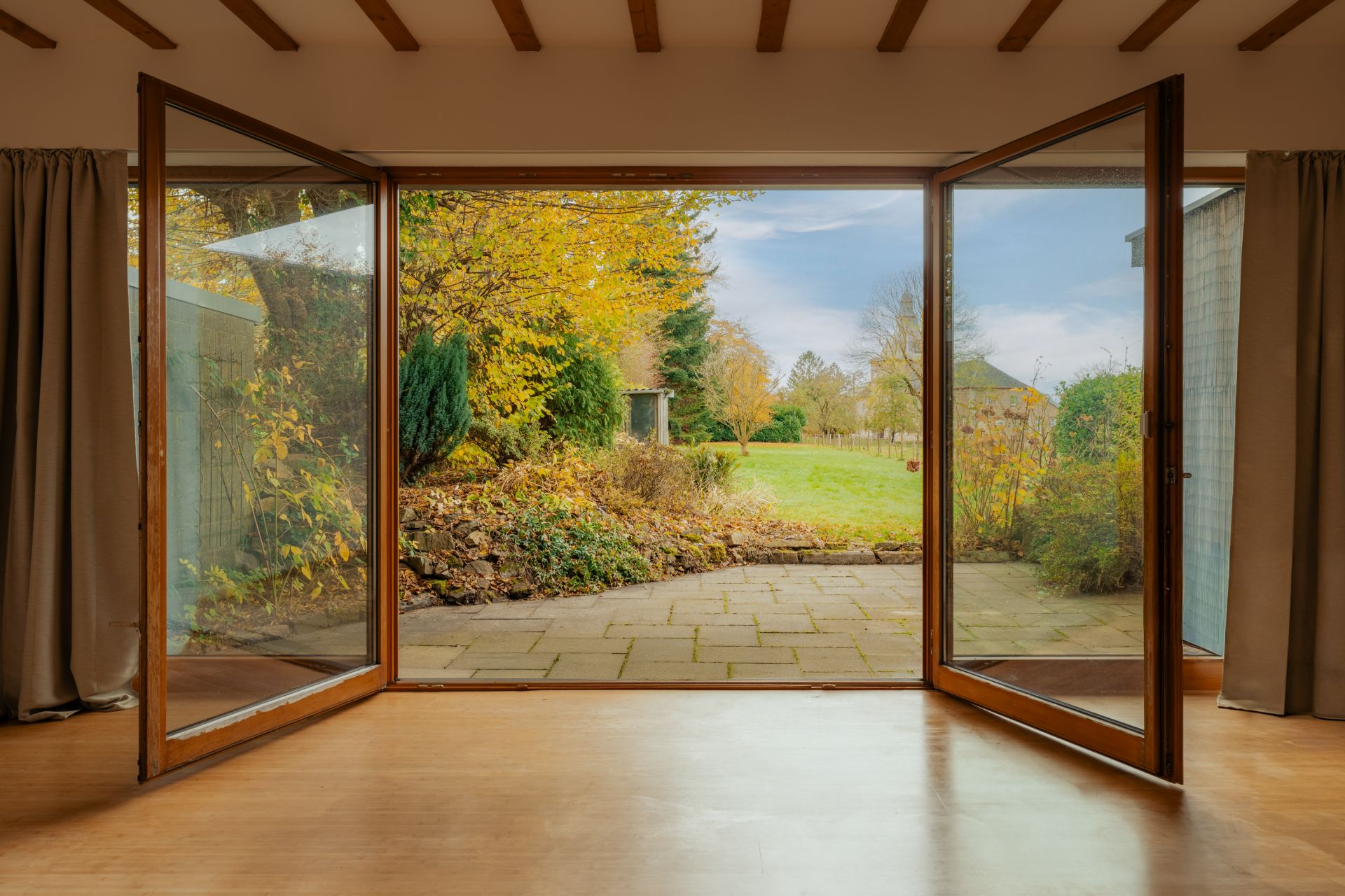 Große Glas-Schiebetüren führen von einem Wohnzimmer auf eine Terrasse mit Gartenblick.