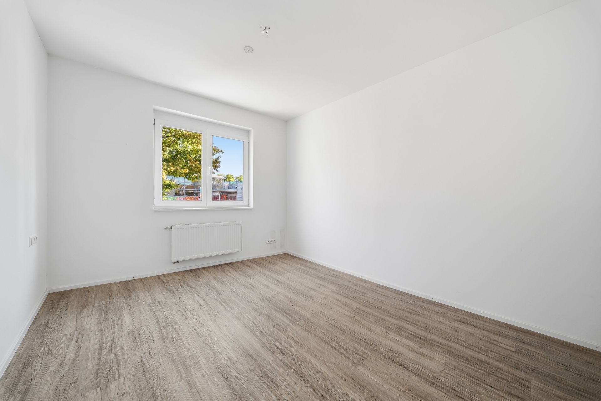 Leeres Zimmer mit weiß gestrichenen Wänden, Fenster und hellem Holzboden.
