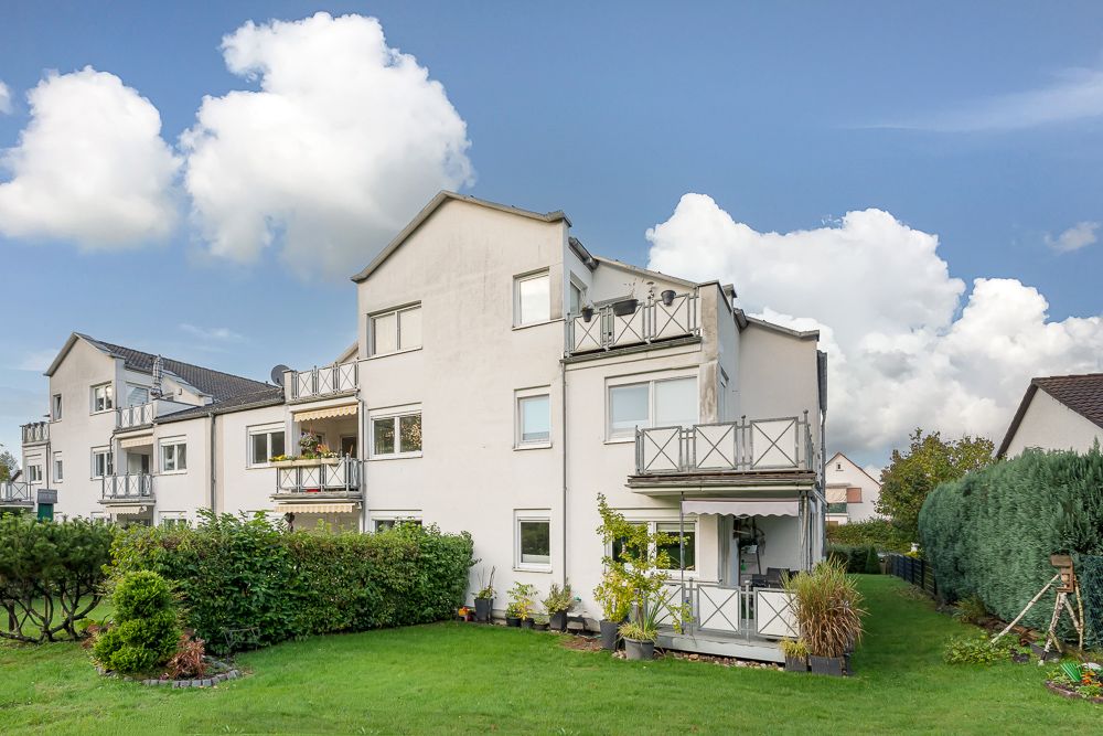 Modernes, weißes Mehrfamilienhaus mit mehreren Balkonen und gepflegtem Garten.