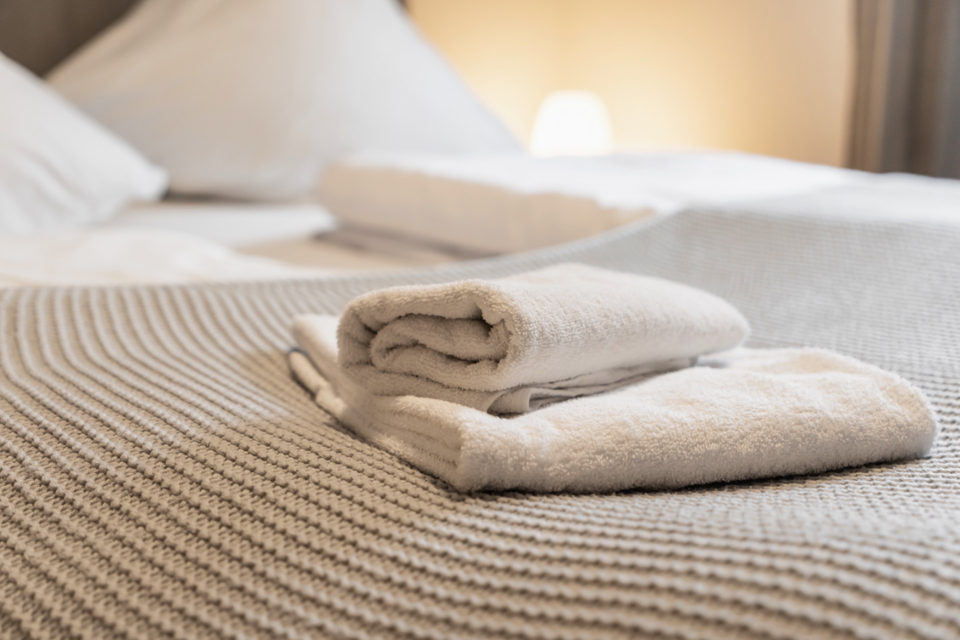 Zwei gefaltete Handtücher liegen auf einem gemachten Bett mit gestrickter Decke.