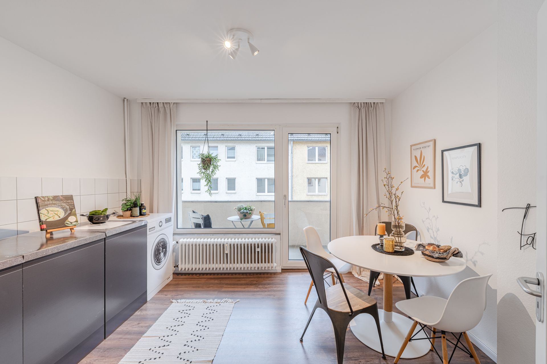 Helle Küche mit Esstisch, Stühlen, Waschmaschine und Zugang zu einem Balkon.