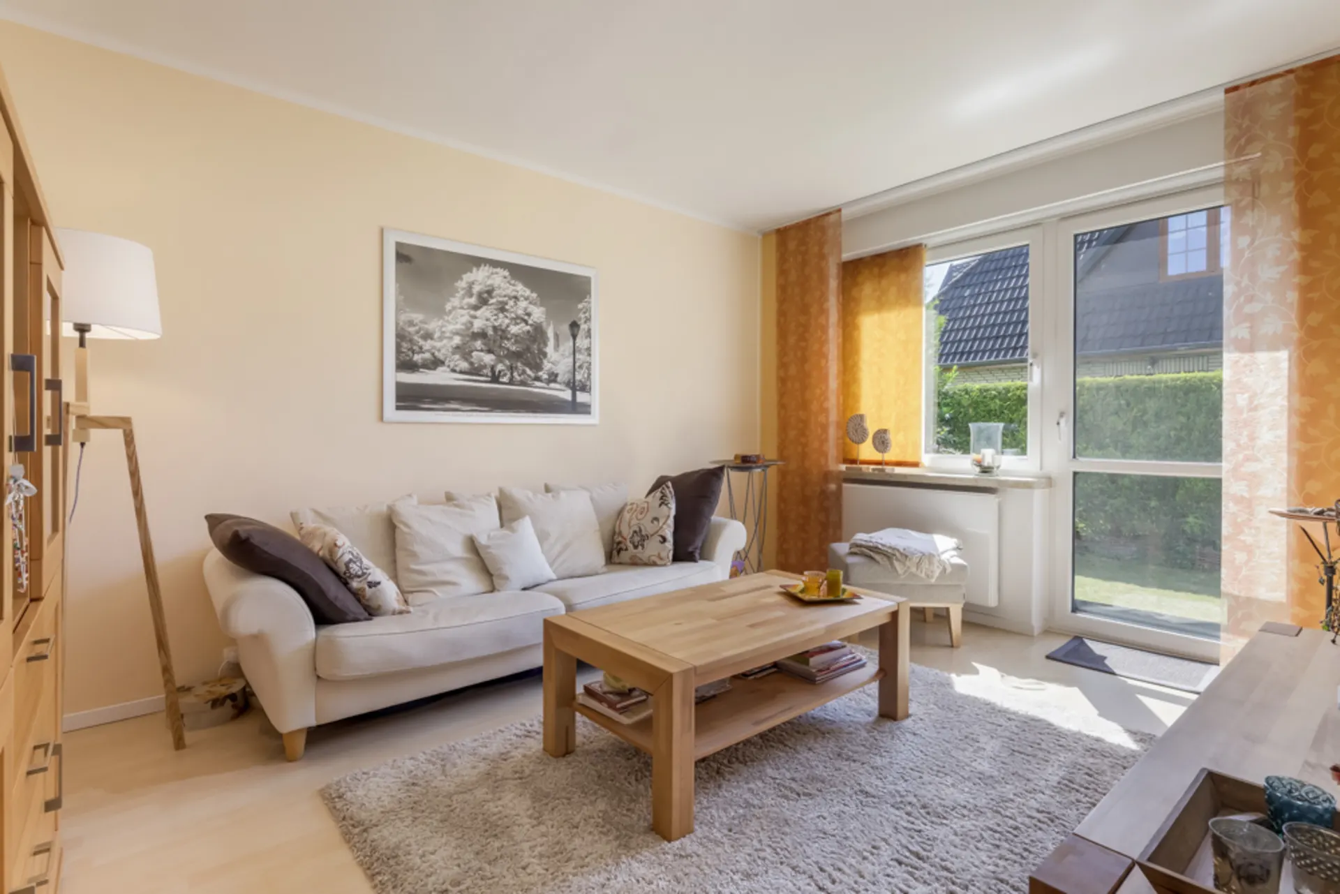 Helles Wohnzimmer mit Sofa, Couchtisch, Teppich und großen Fenstern mit Blick in den Garten.