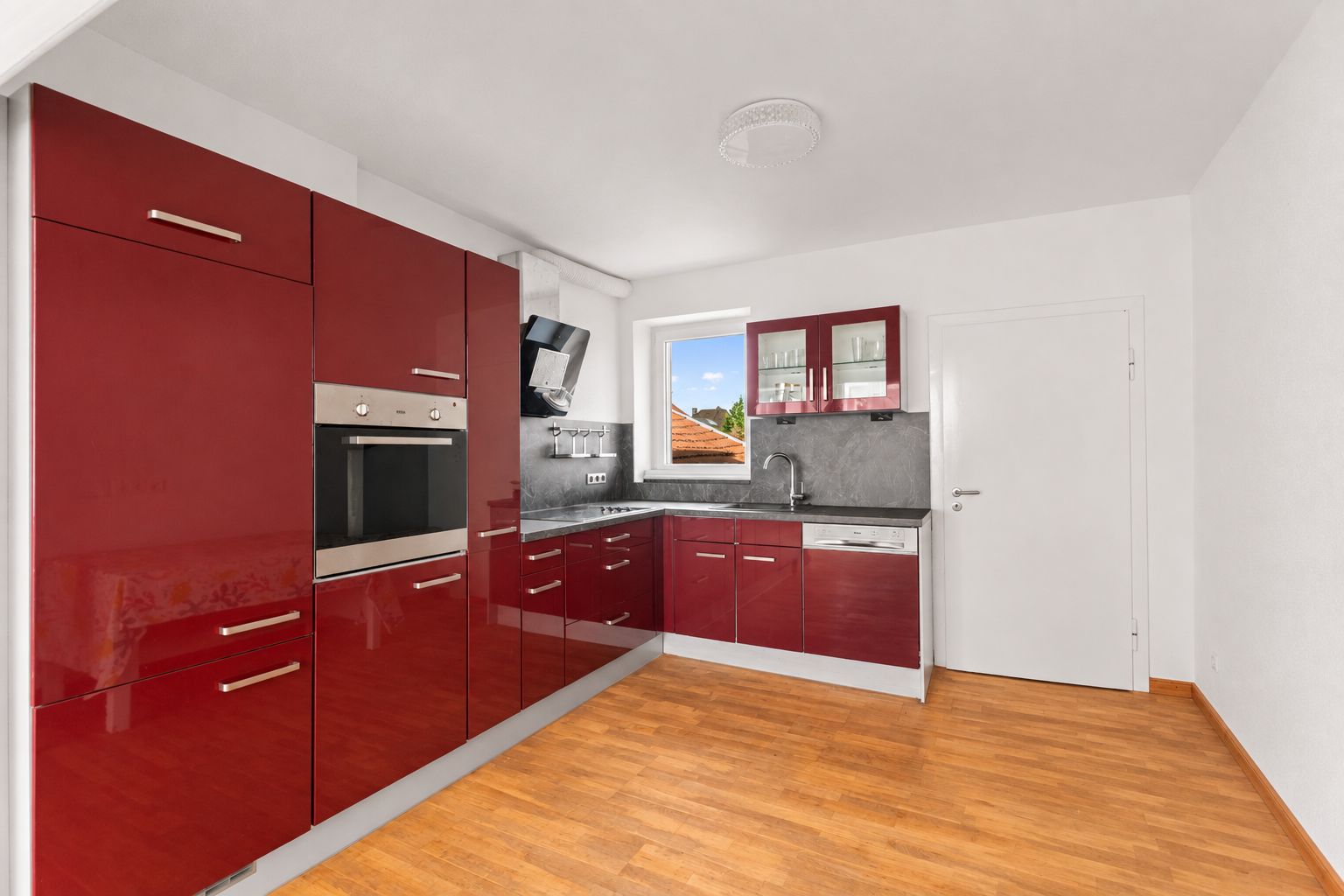 Moderne Einbauküche mit roten Hochglanzfronten, grauer Arbeitsplatte und Holzfußboden.