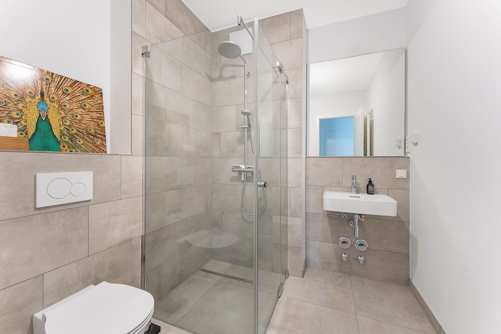 Modernes Badezimmer mit Dusche, WC, Waschbecken und Spiegel, dekoriert mit einem Bild von einem Pfau.