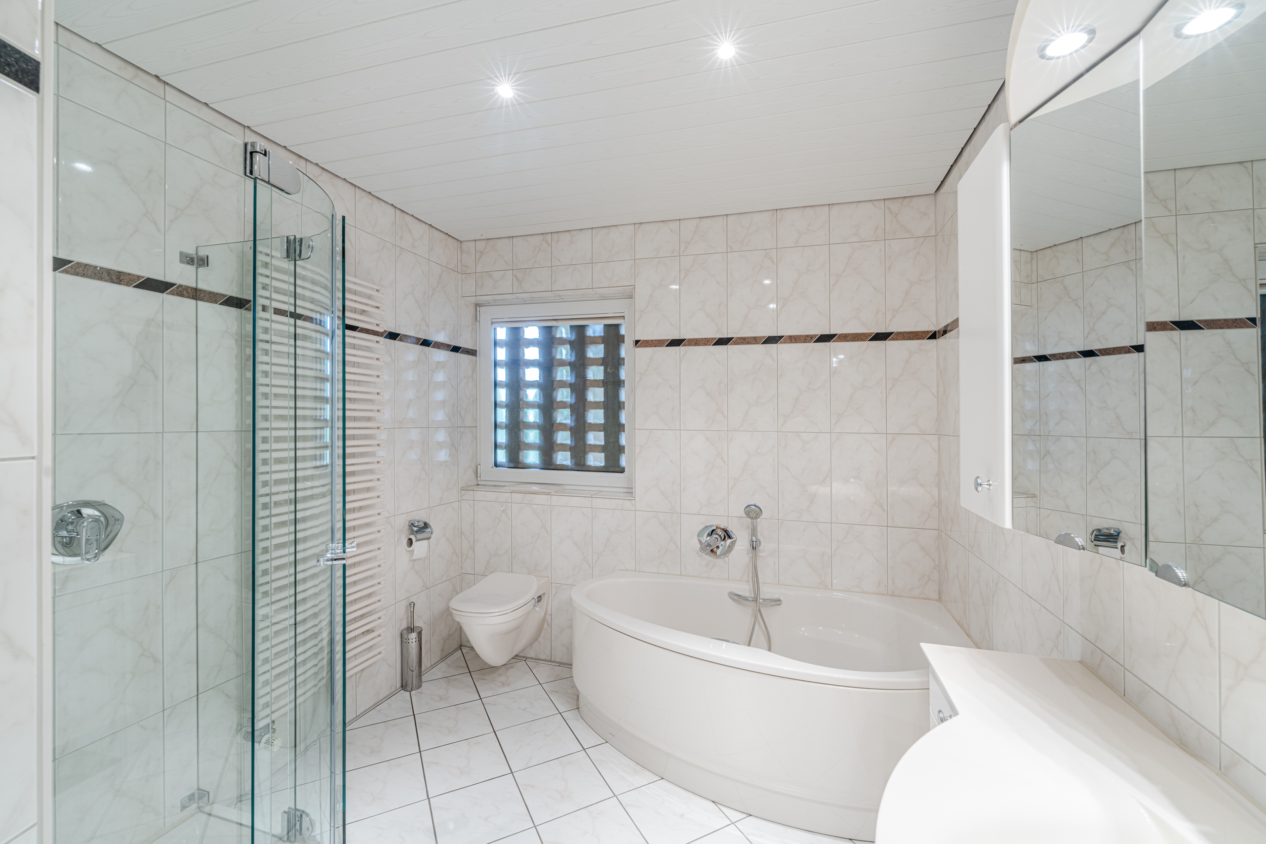 Modernes Badezimmer mit Eckbadewanne, Dusche aus Glas, WC und großem Spiegel.