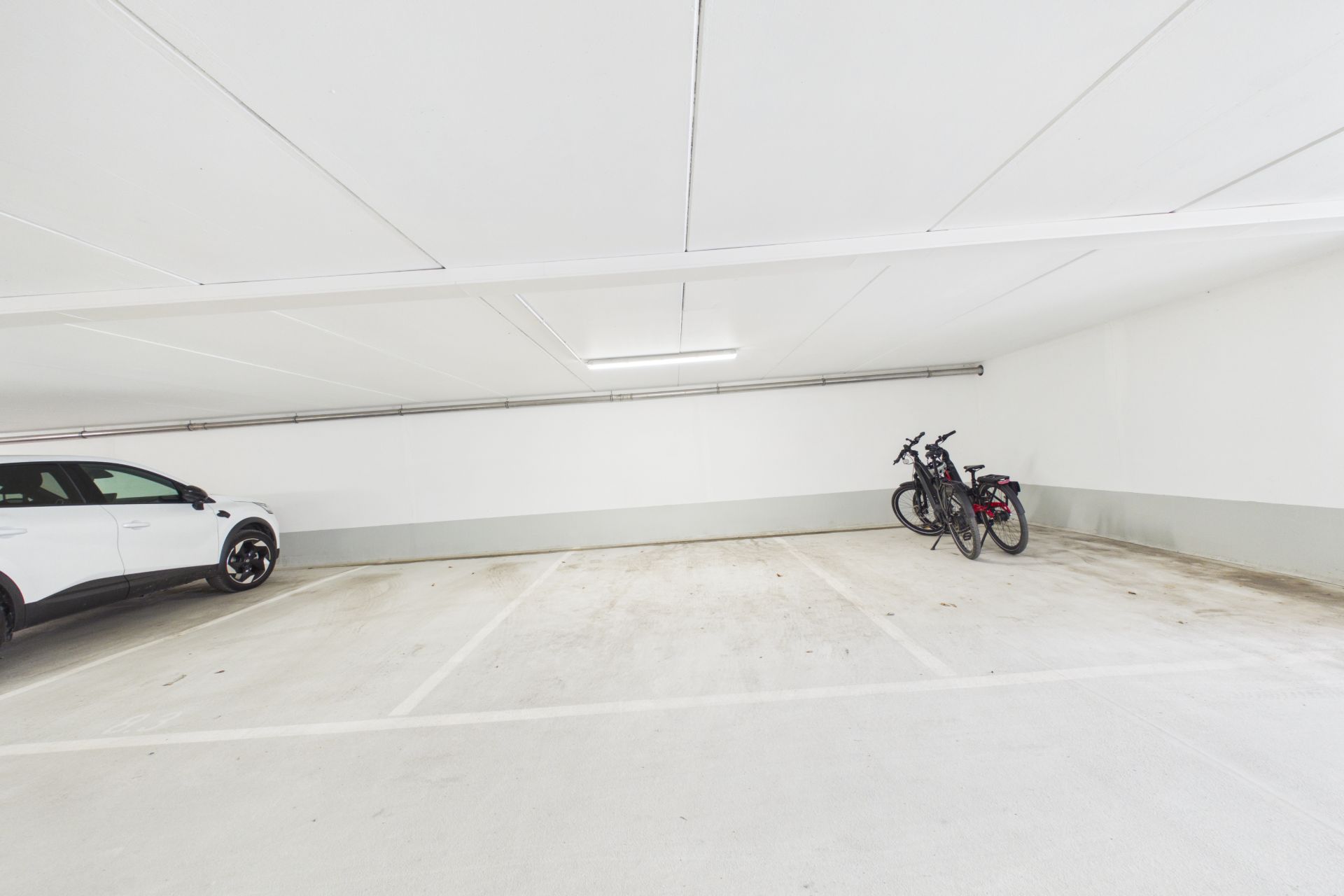 Helle Tiefgarage mit einem weißen Auto und zwei Fahrrädern an der Wand.