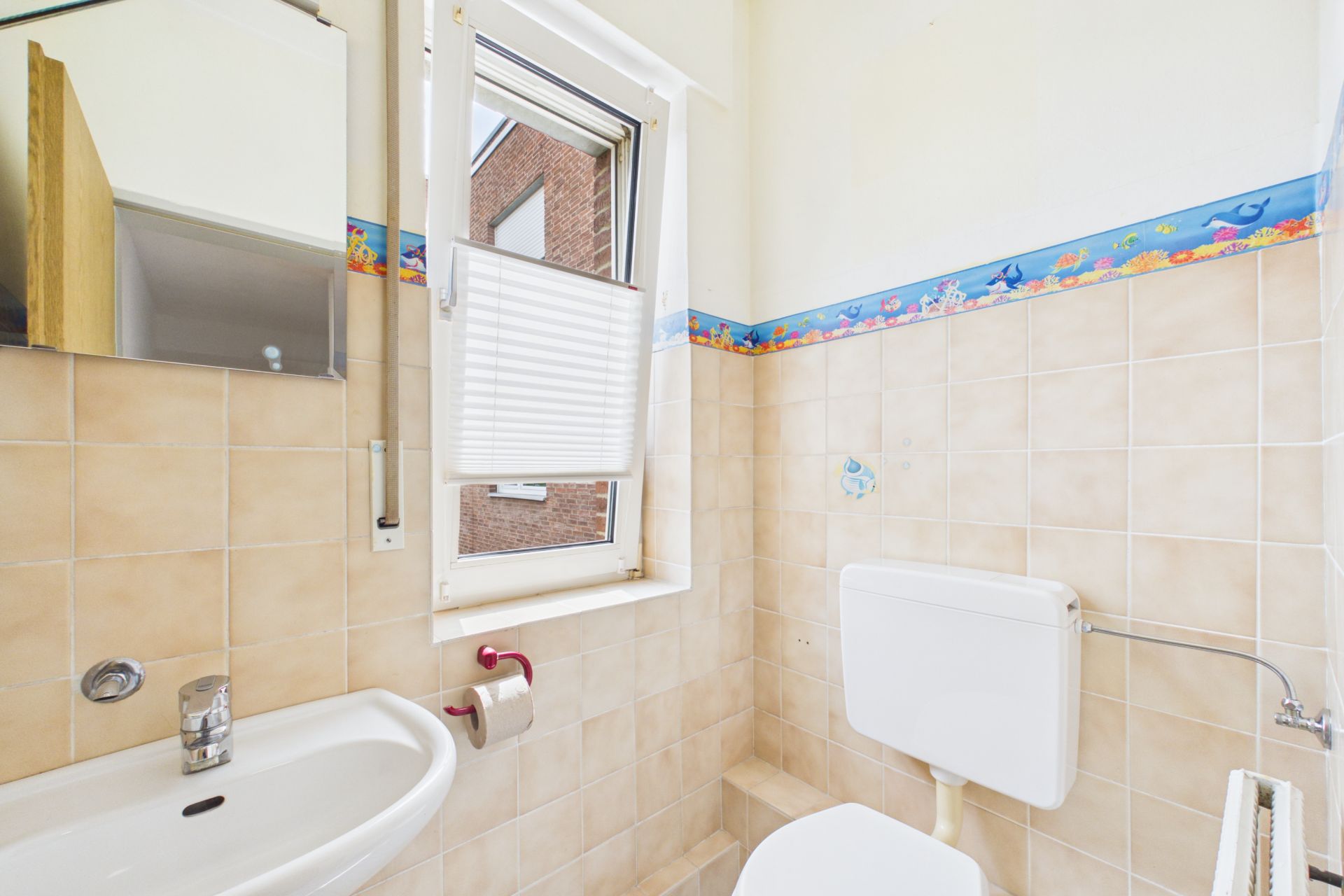 Kleines Badezimmer mit Waschbecken, Toilette, Fenster und maritimer Bordüre an den Fliesen.