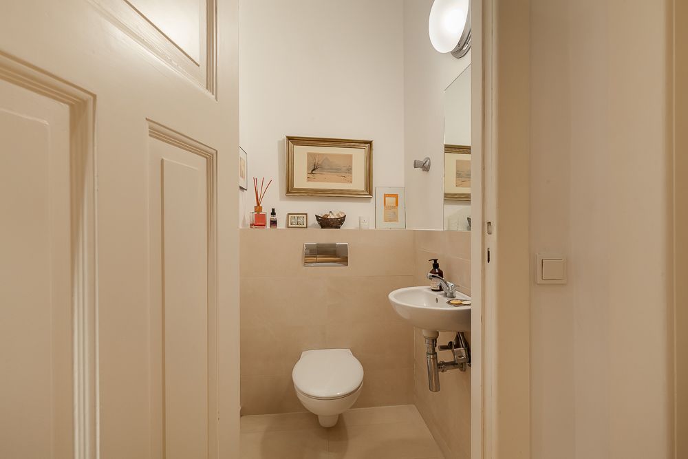 Kleines Badezimmer mit Wandtoilette, kleinem Waschbecken und Bildern an der Wand.