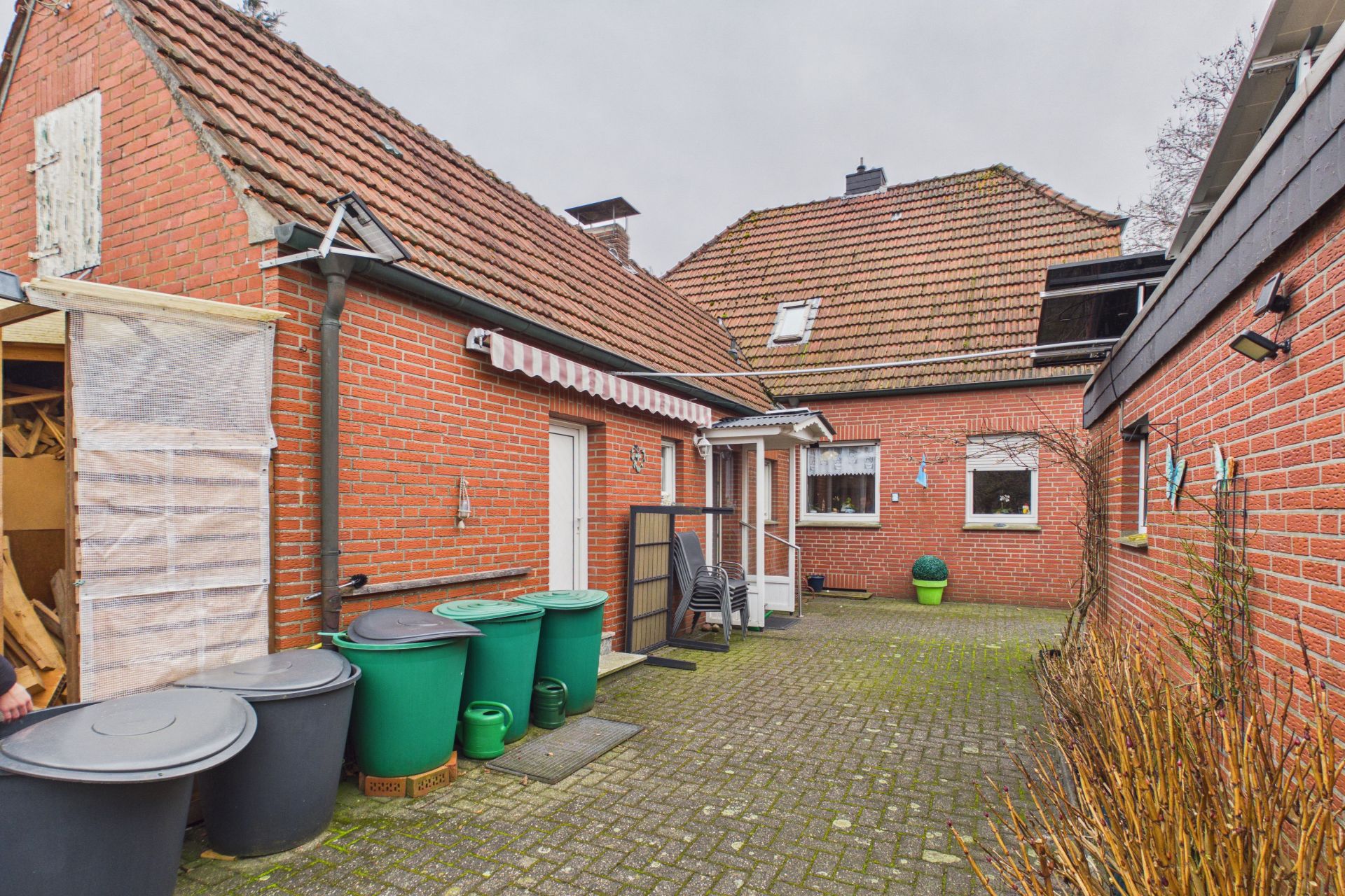 Innenhof mit roten Backsteinwänden, mehreren grünen Mülltonnen und gepflastertem Boden.