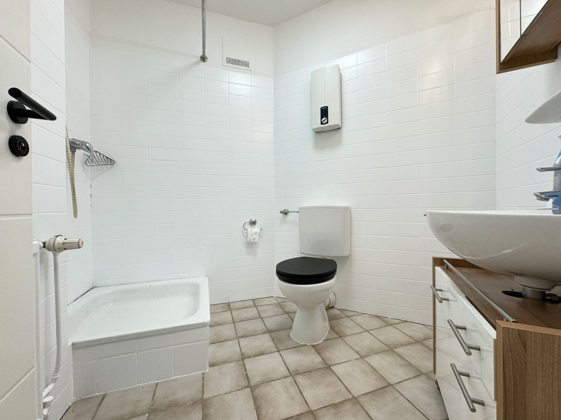 Helles Badezimmer mit Dusche, Toilette, Waschbecken und Fliesenboden.