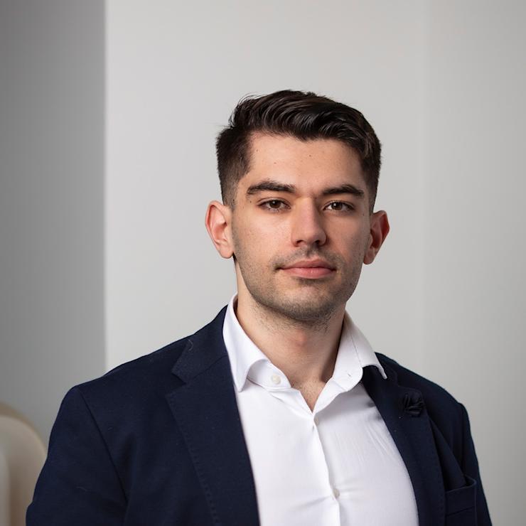 Ein junger Mann im Anzug steht vor einer hellen Wand.