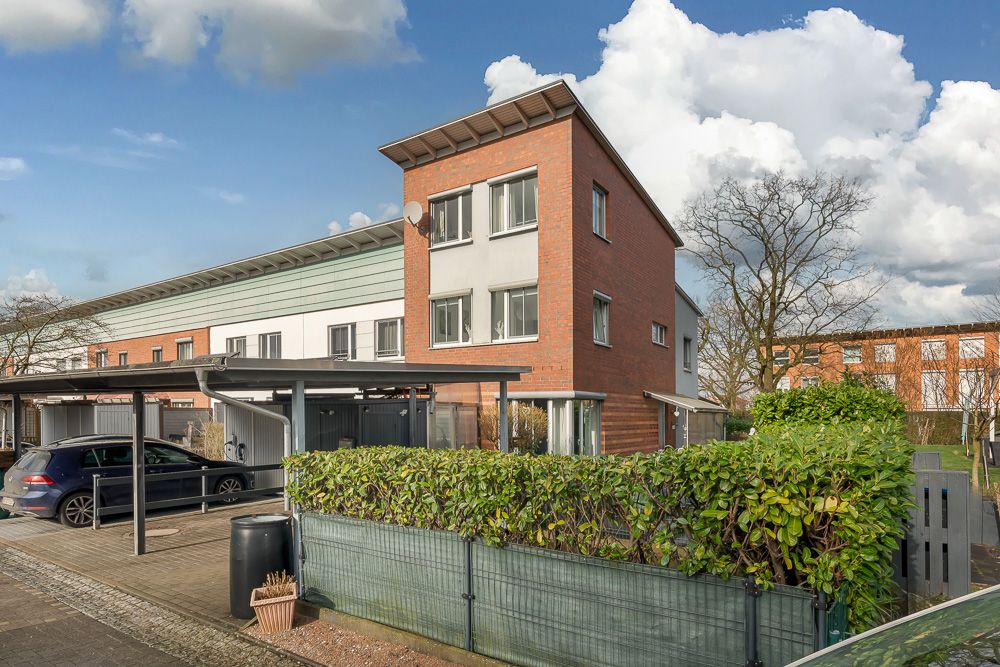 Modernes Reihenhaus mit drei Stockwerken, Klinkerfassade, Carport und grüner Hecke im Vordergrund.