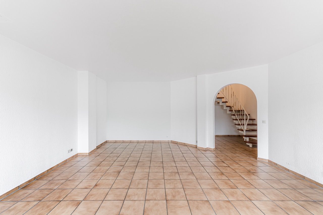 Leeres Zimmer mit gefliestem Boden und Treppe hinter einem Rundbogen.