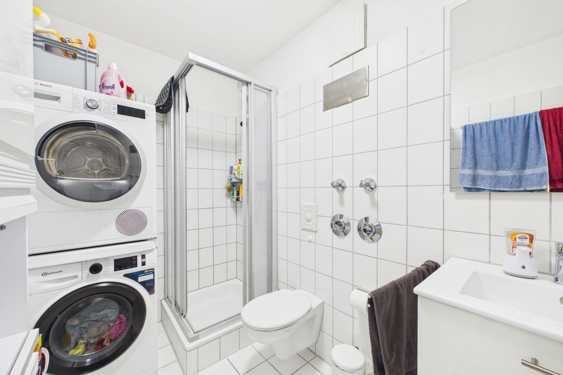 Helles Badezimmer mit Dusche, WC, Waschbecken und gestapelter Waschmaschine und Trockner.