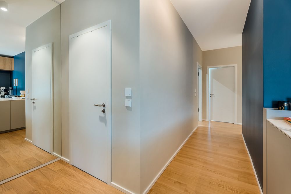 Moderner Flur mit Holzboden, weißen Türen und Spiegelwand, angrenzende Küche sichtbar.