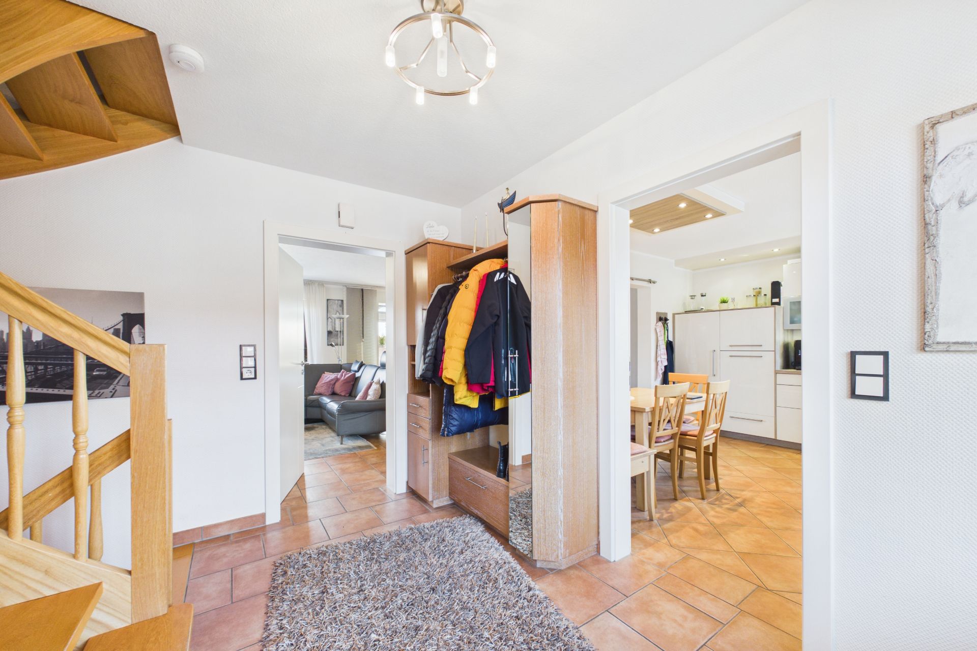 Heller Flur mit Garderobe, Treppe, Teppich und Blick in Wohnzimmer und Küche.