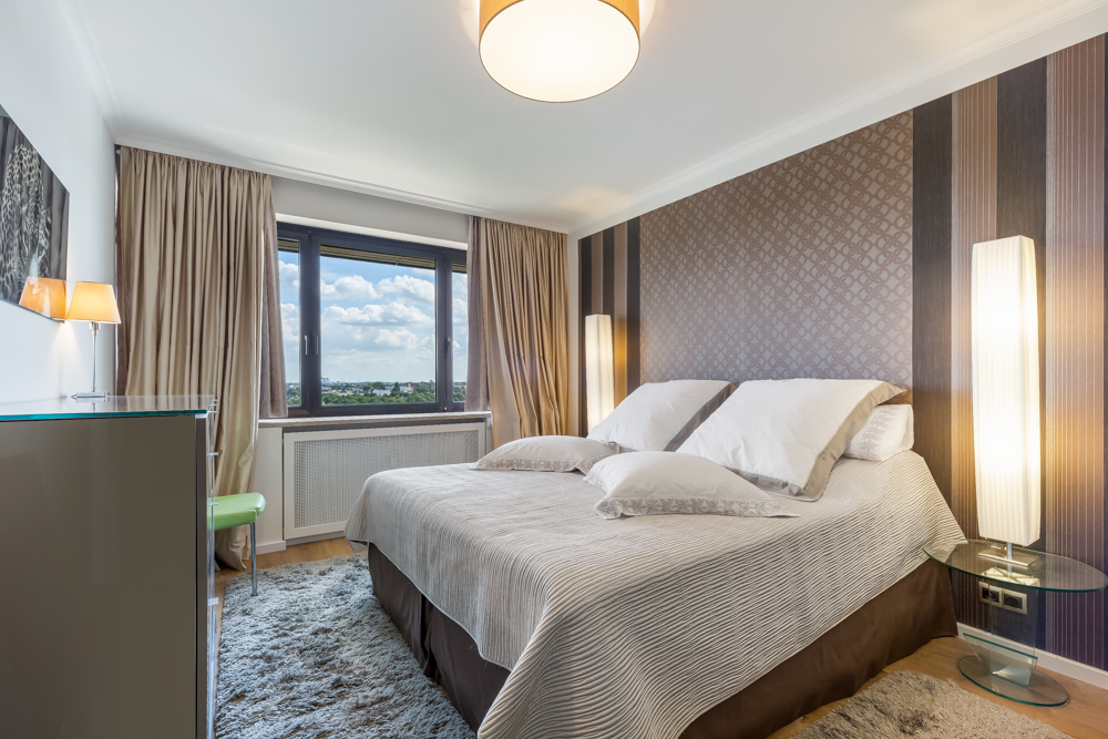 Modernes Schlafzimmer mit Doppelbett, großen Fenstern und gemusterter Tapete.
