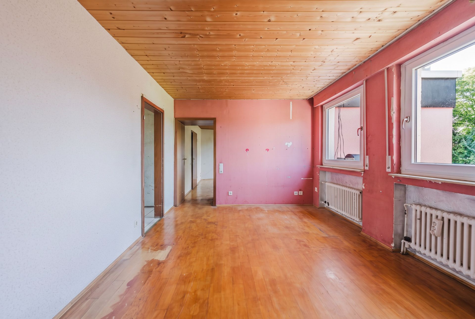 Leerer Raum mit Holzdecke, Holzboden, rosa Wänden und zwei großen Fenstern.
