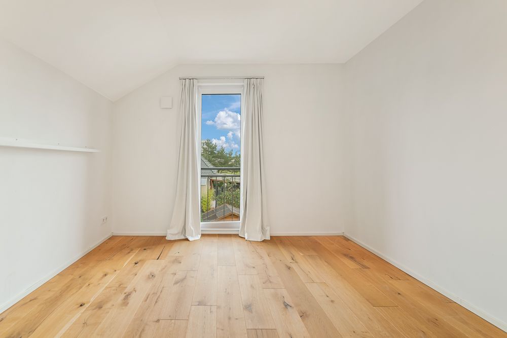 Leeres Zimmer mit weißer Wand, Holzboden und Fenster mit weißen Vorhängen.
