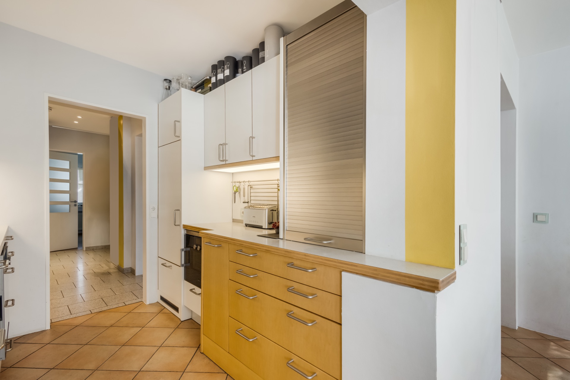 Moderne Küche mit Holzschränken, weißen Oberschränken und gelbem Wandstreifen.