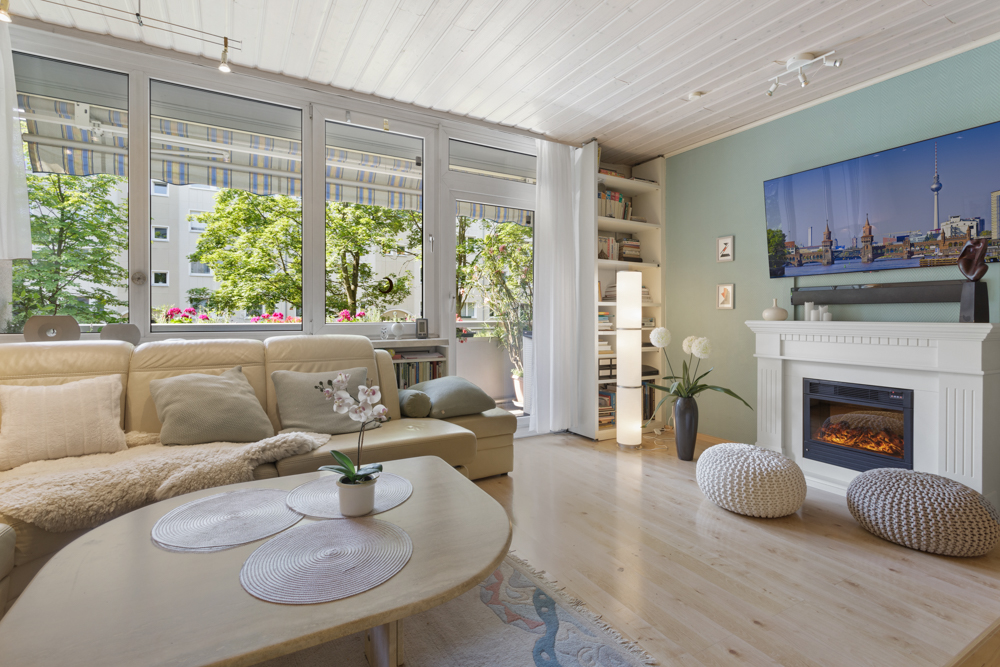 Helles Wohnzimmer mit Sofa, Kamin, großem Fenster, Couchtisch und Dekorationen.