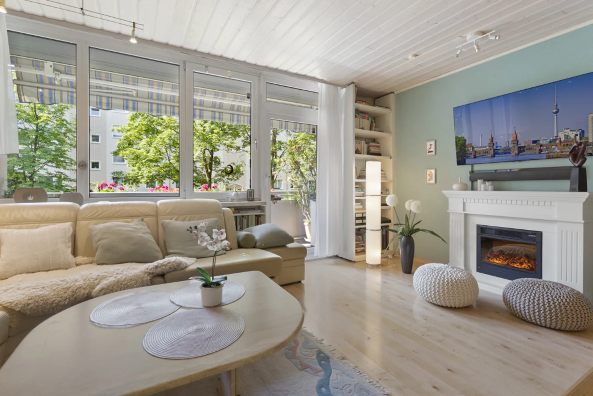 Helles Wohnzimmer mit Sofa, Kamin, großem Fenster, Couchtisch und Dekorationen.
