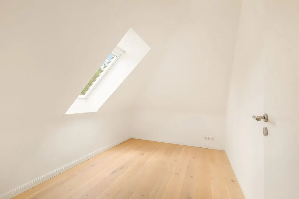 Leerer, heller Raum mit Holzfußboden und schrägem Dachfenster.