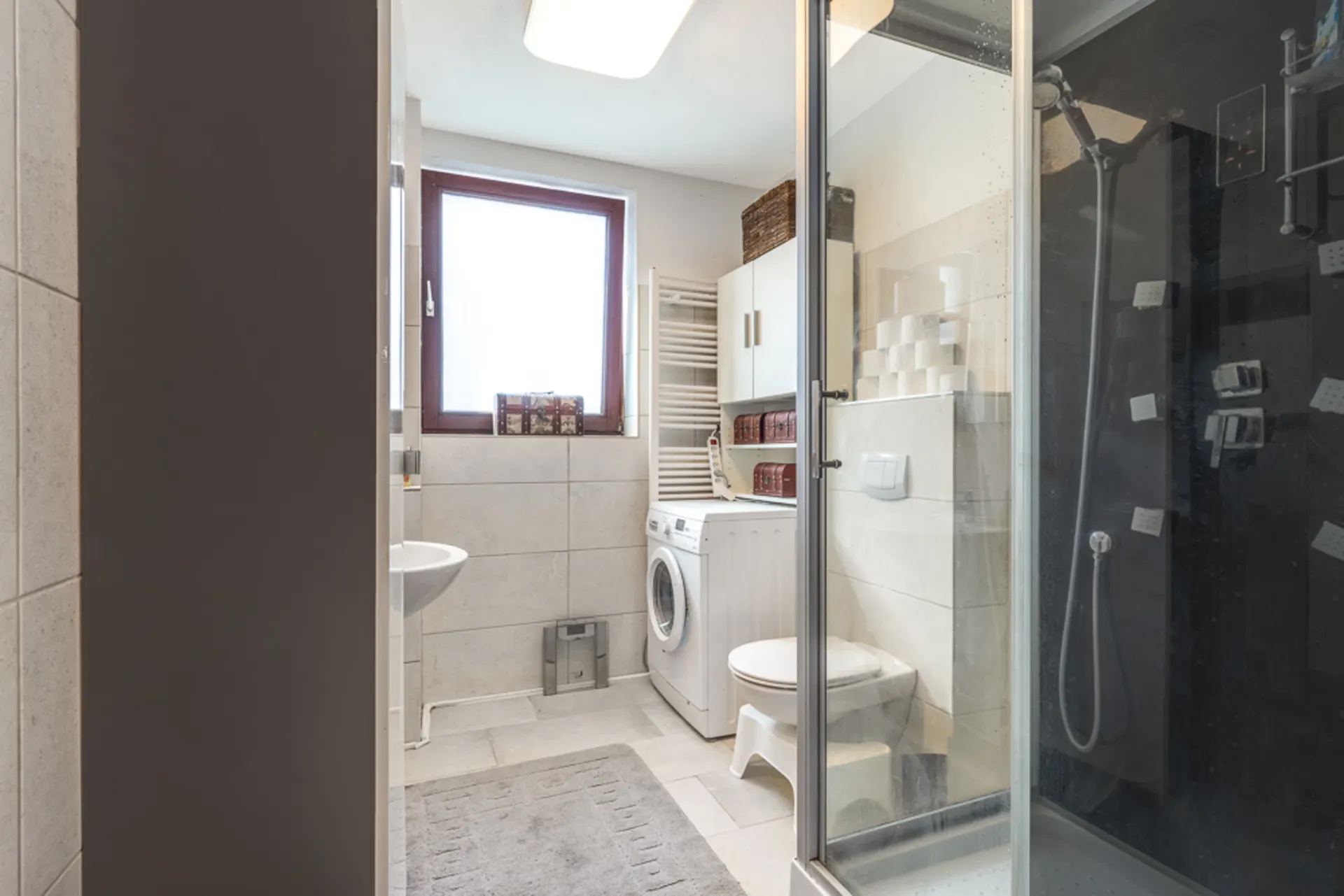 Modernes Badezimmer mit Dusche, Waschmaschine, WC und Fenster.