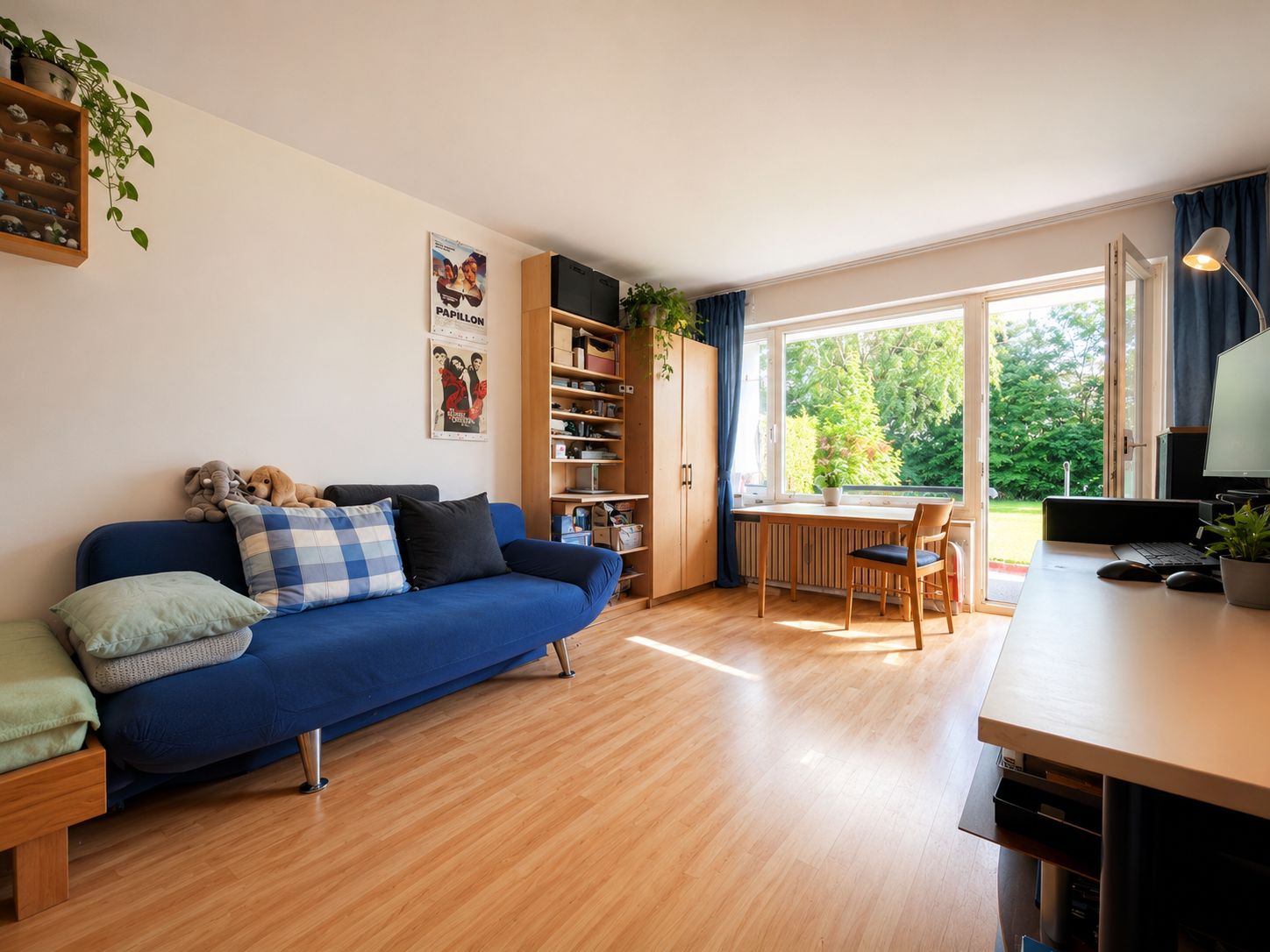 Helles Wohnzimmer mit Sofa, Schreibtisch und großem Fenster zum Garten.