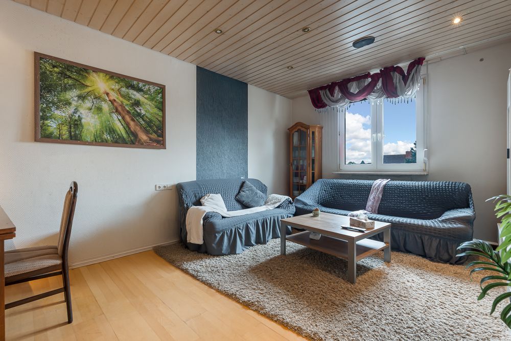 Wohnzimmer mit zwei Sofas, Couchtisch, großem Fenster und Wandbild eines Baumes.
