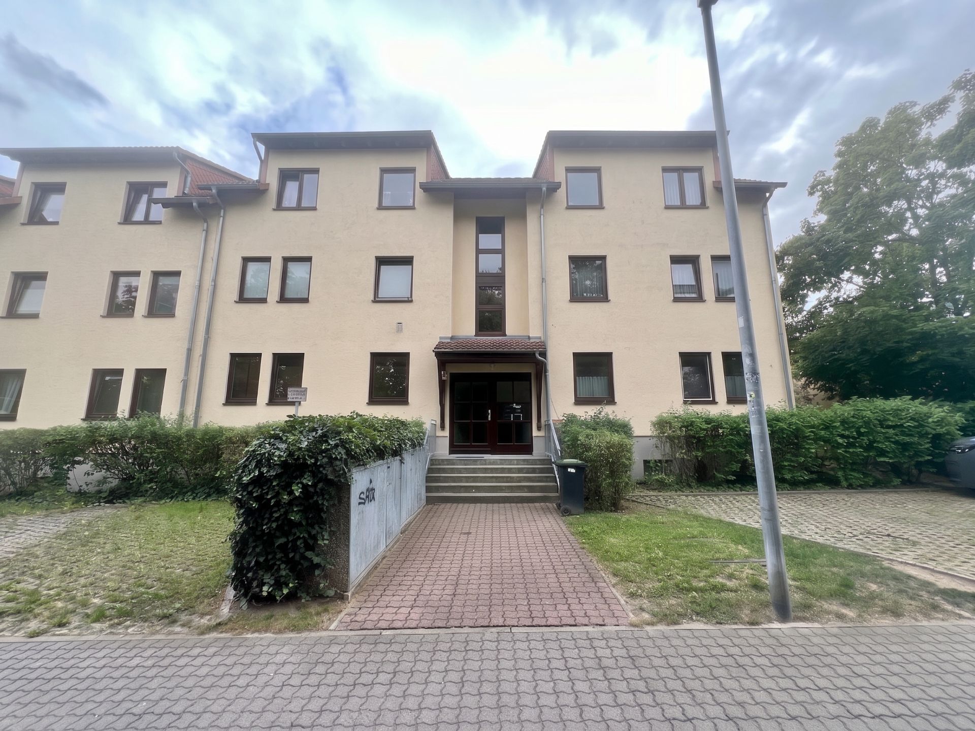 Mehrfamilienhaus mit drei Etagen, Eingangsbereich mit Treppe und Vorgarten.