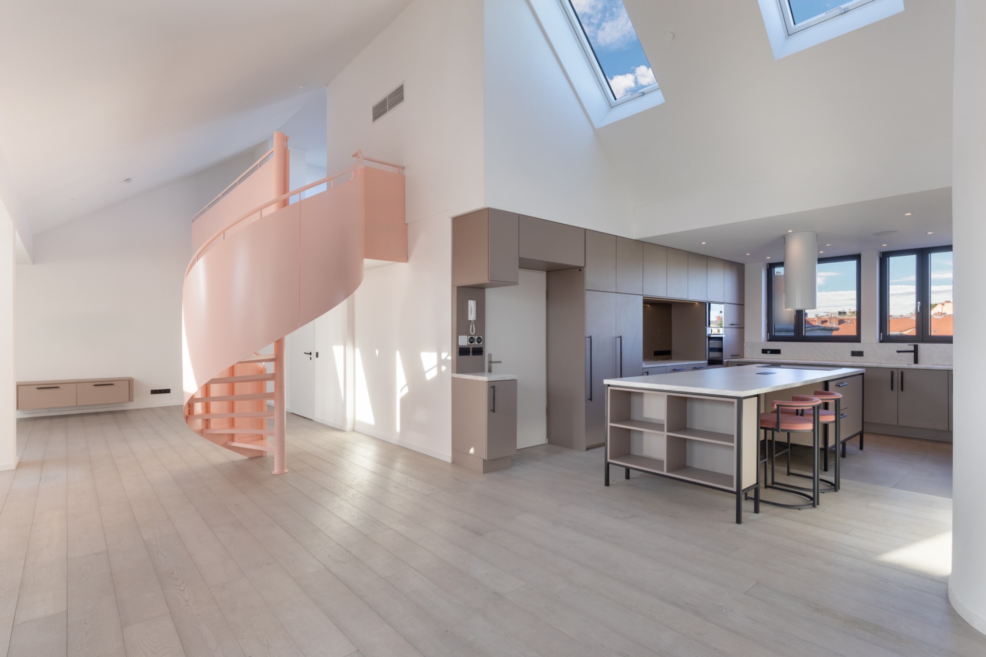 Moderne helle Wohnküche mit Kücheninsel und rosa Wendeltreppe, große Fenster im Dach.