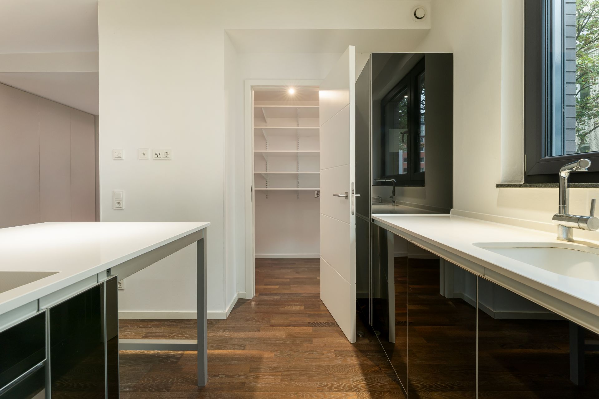 Moderne Küche mit Holzboden, weißem Tresen und Blick auf Vorratsraum mit Regalen.