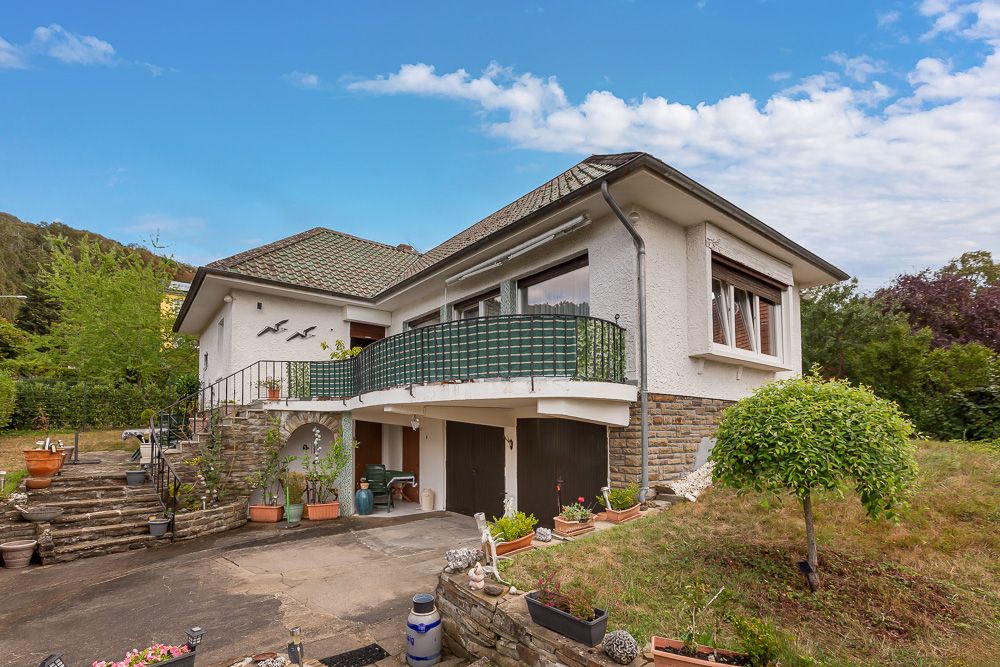 Zweistöckiges Wohnhaus mit Balkon, Garage und Vorgarten, umgeben von Grünflächen.