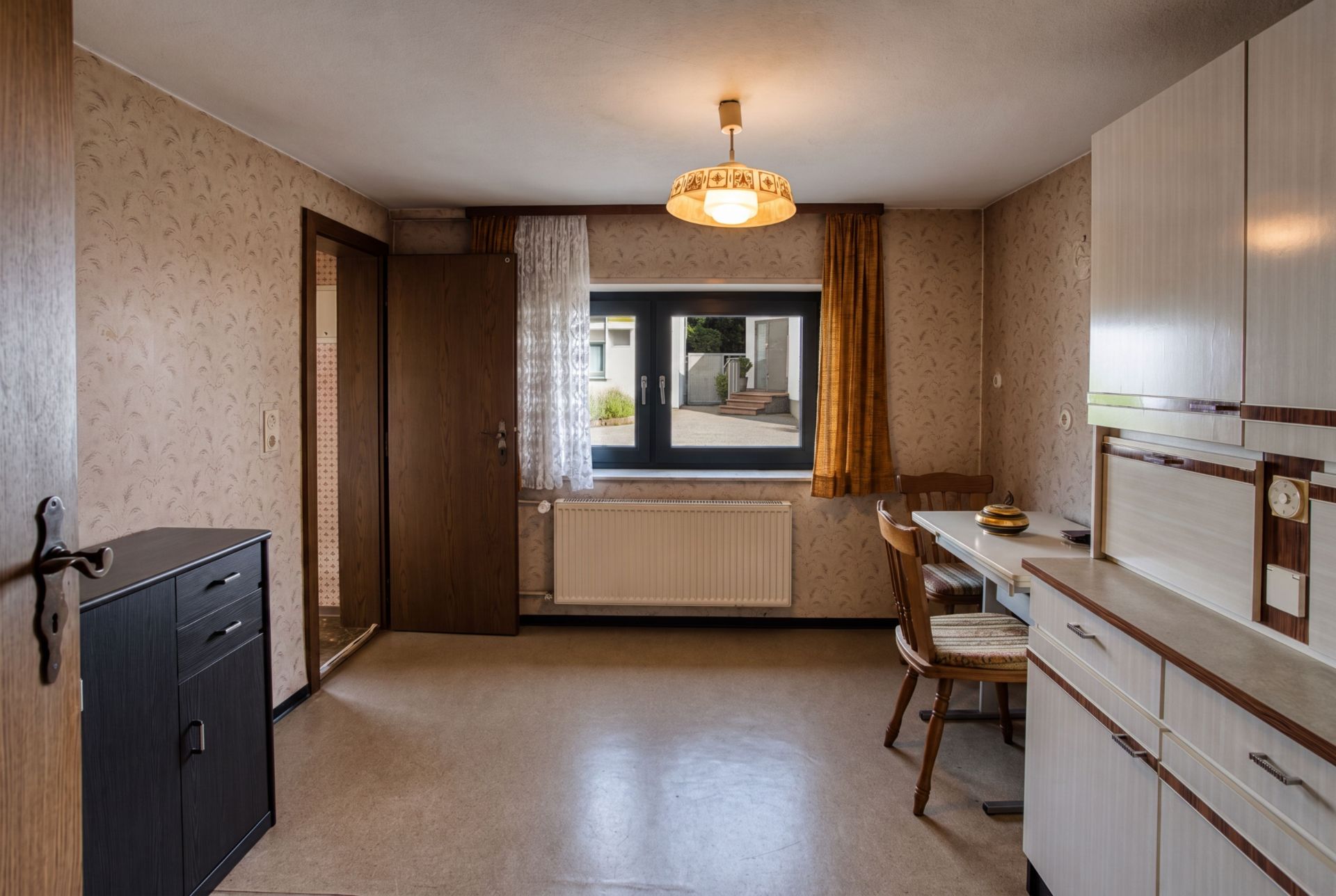 Heller Raum mit Fenster, Tisch, Stühlen, Sideboard und Deckenlampe in einer Wohnung.
