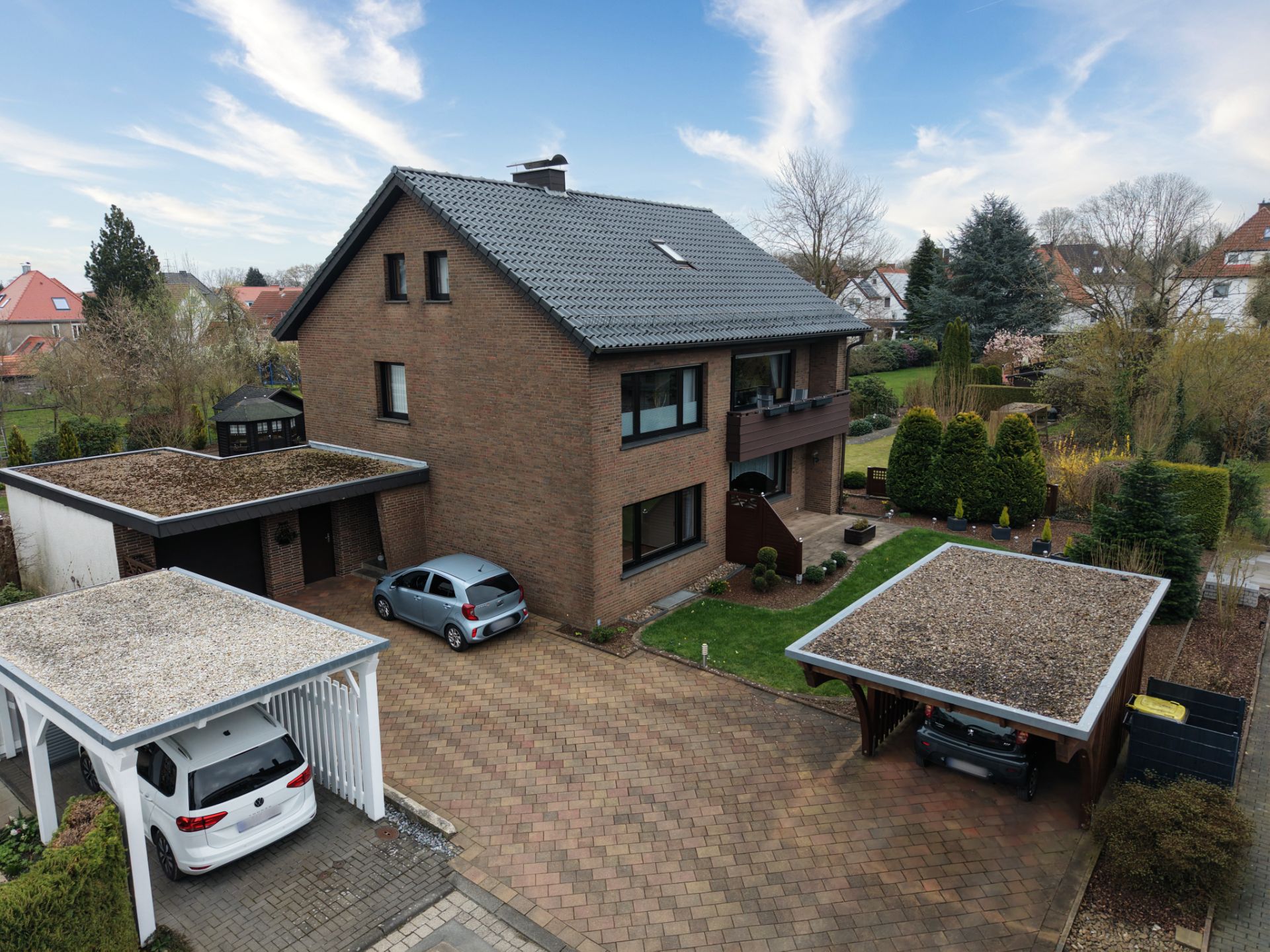Backsteinwohnhaus mit drei Garagen, zwei Autos und gepflegtem Garten im Hof.
