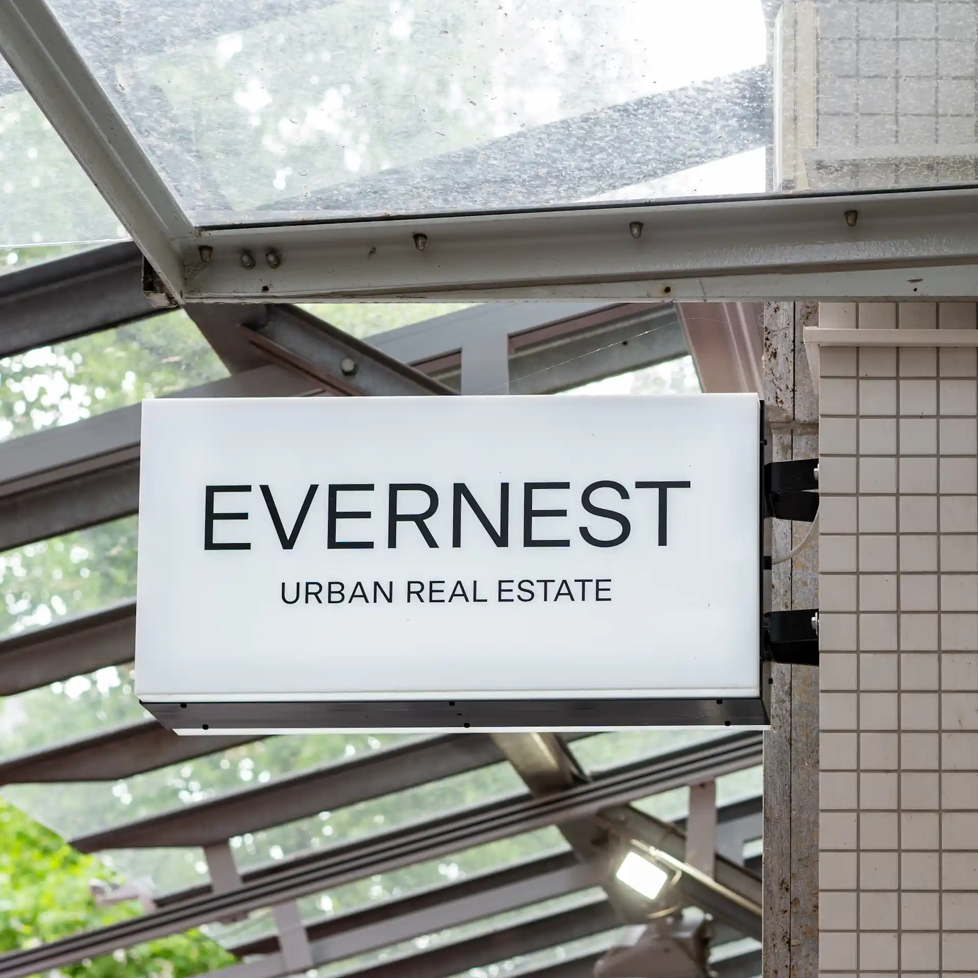 Leuchtreklame mit der Aufschrift 'EVERNEST URBAN REAL ESTATE' an einer Hauswand.