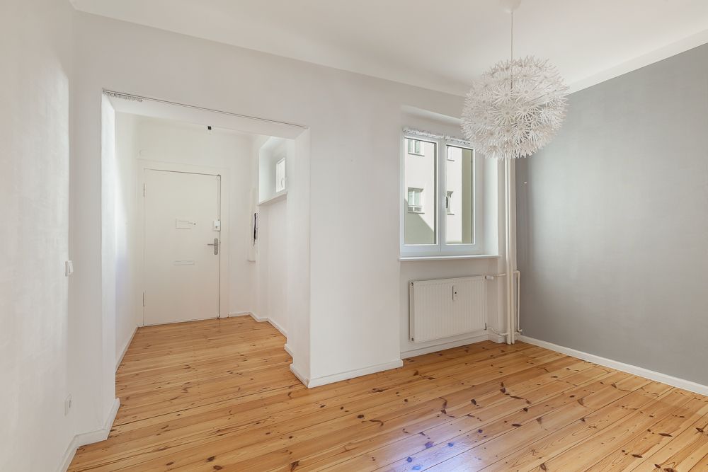 Heller Raum mit Holzboden, Fenster, weißer Tür und moderner Lampe an der Decke.