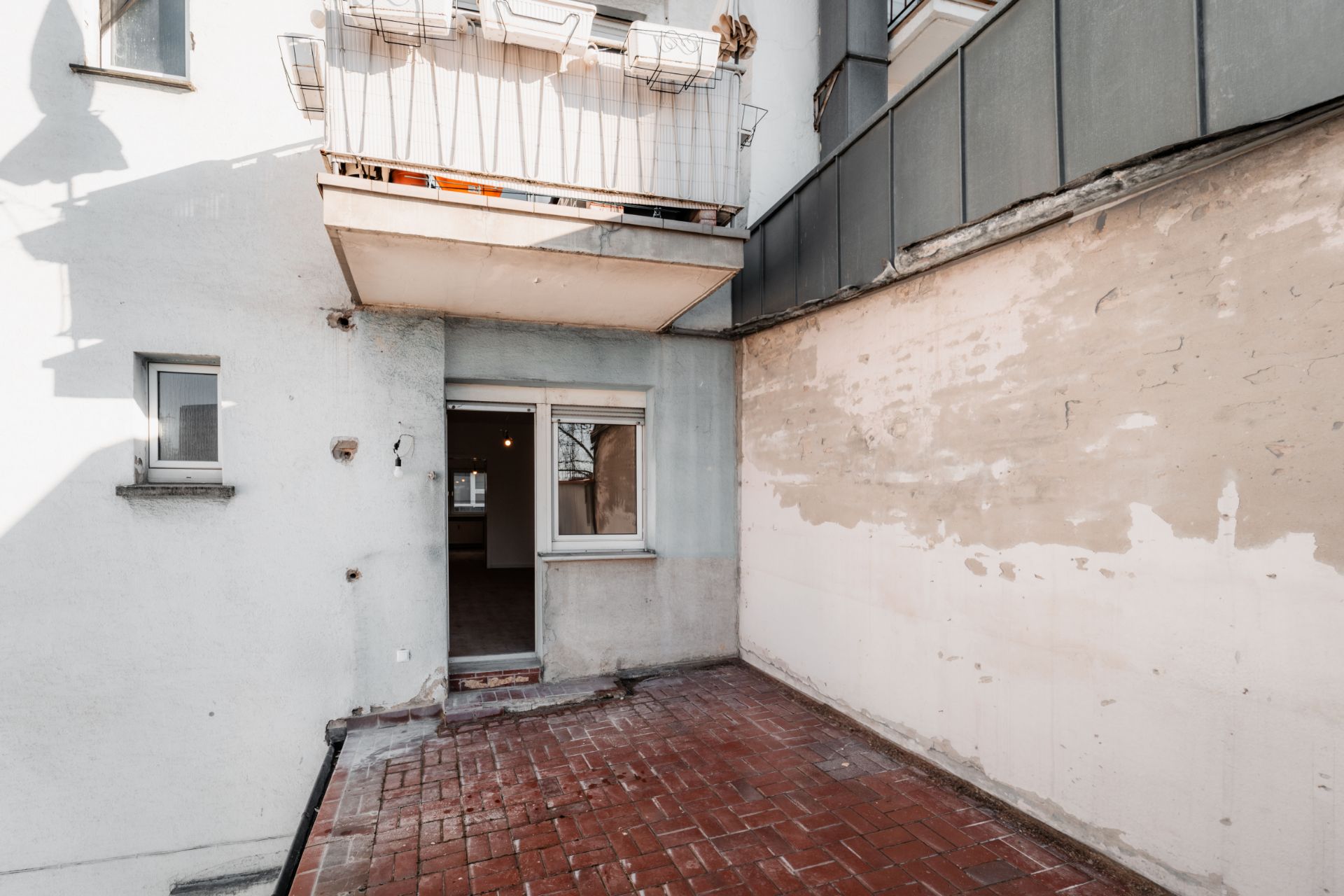 Offene Terrasse mit rotem Fliesenboden und Zugangstür zu einer Wohnung.