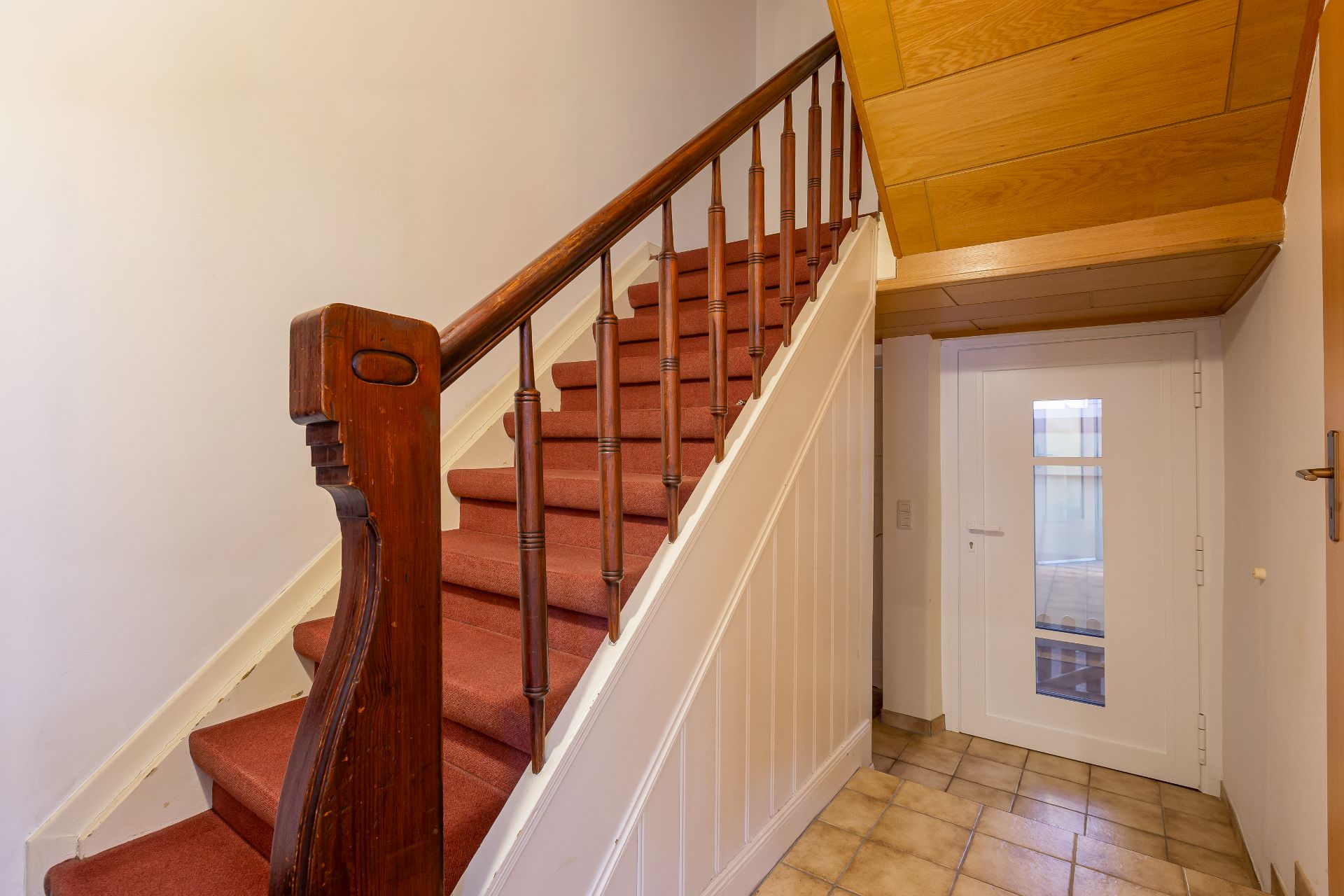 Treppe mit rotem Teppich, Holzgeländer und weißer Tür im Eingangsbereich.