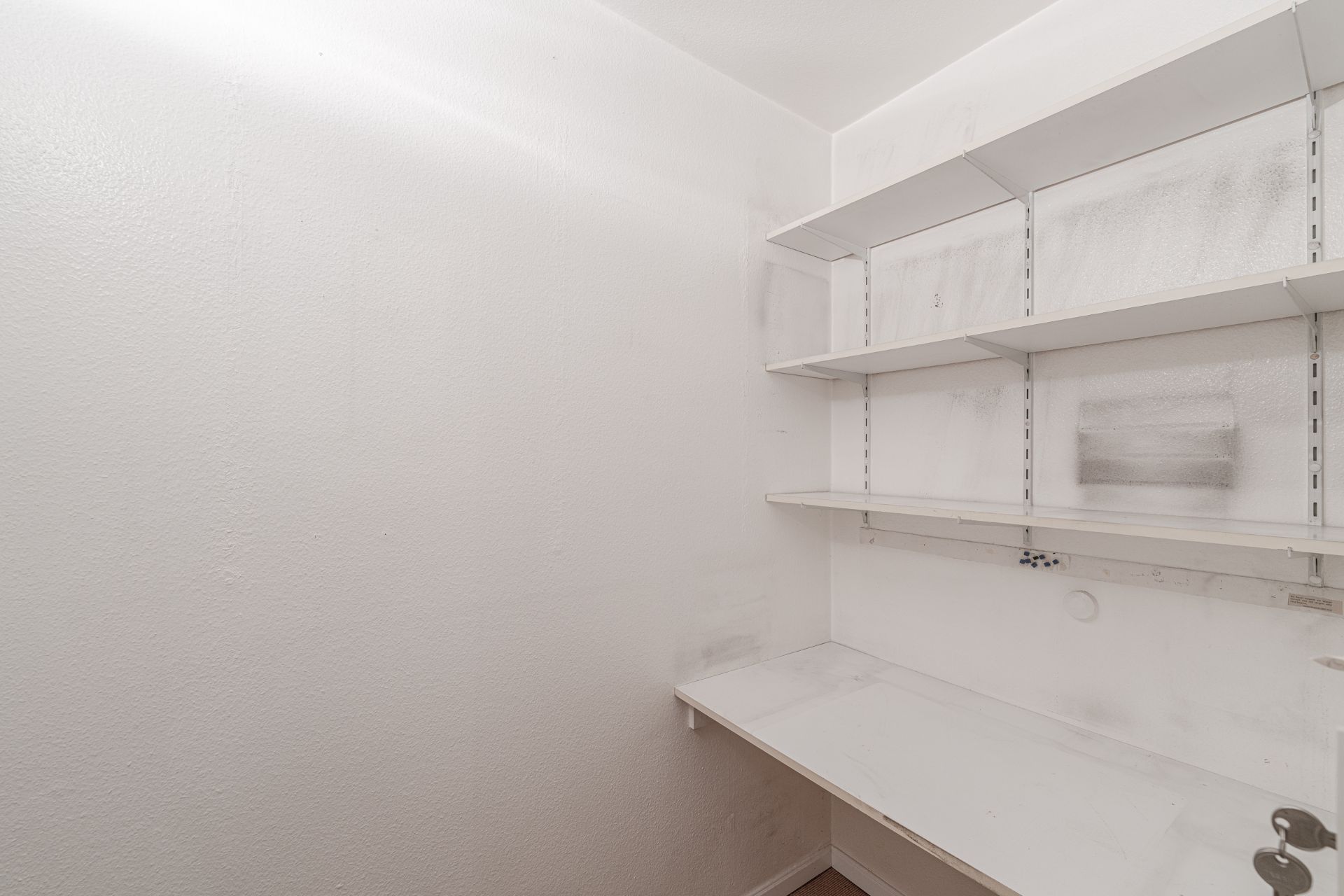 Kleiner Raum mit weißen Regalböden an der Wand und einer weißen Arbeitsfläche.