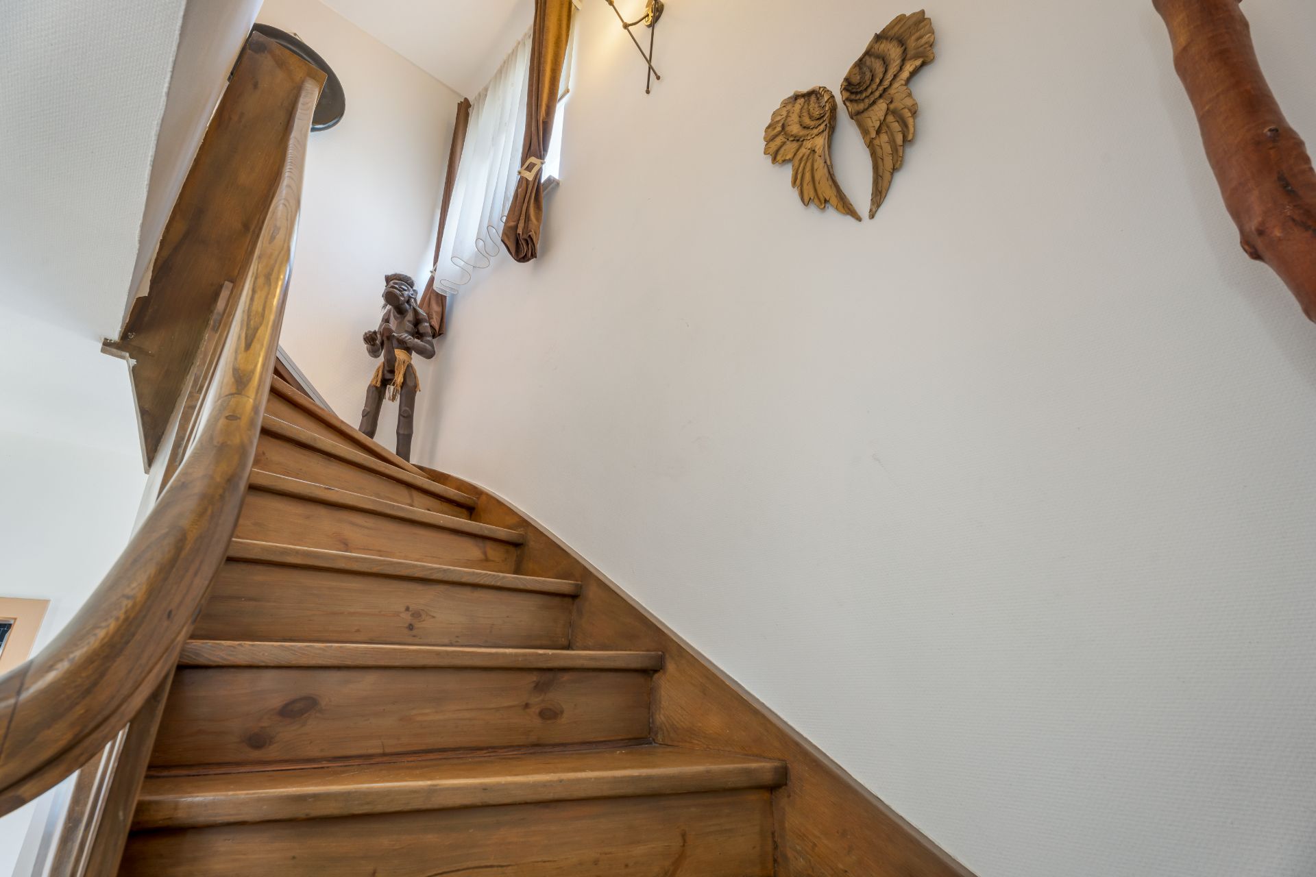 Holztreppe mit Handlauf, Wanddeko in Form von Flügeln und Figur am oberen Treppenabsatz.