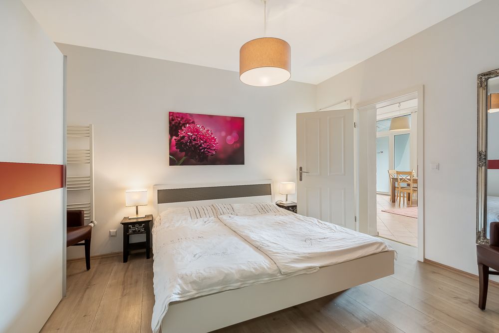Helles Schlafzimmer mit Doppelbett, Nachttischen, Lampen und Blumenbild an der Wand.