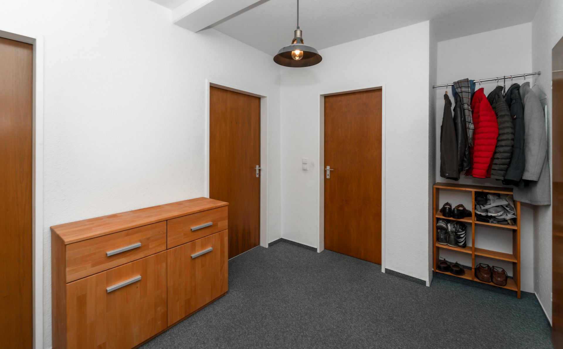 Flur mit drei Holztüren, Kommode, Garderobe mit Jacken und Regal mit Schuhen.