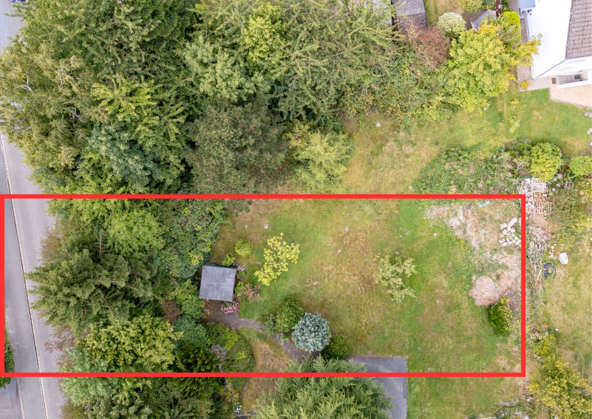 Luftaufnahme eines rechteckigen Gartengrundstücks mit Bäumen, Rasen und kleinem Schuppen.