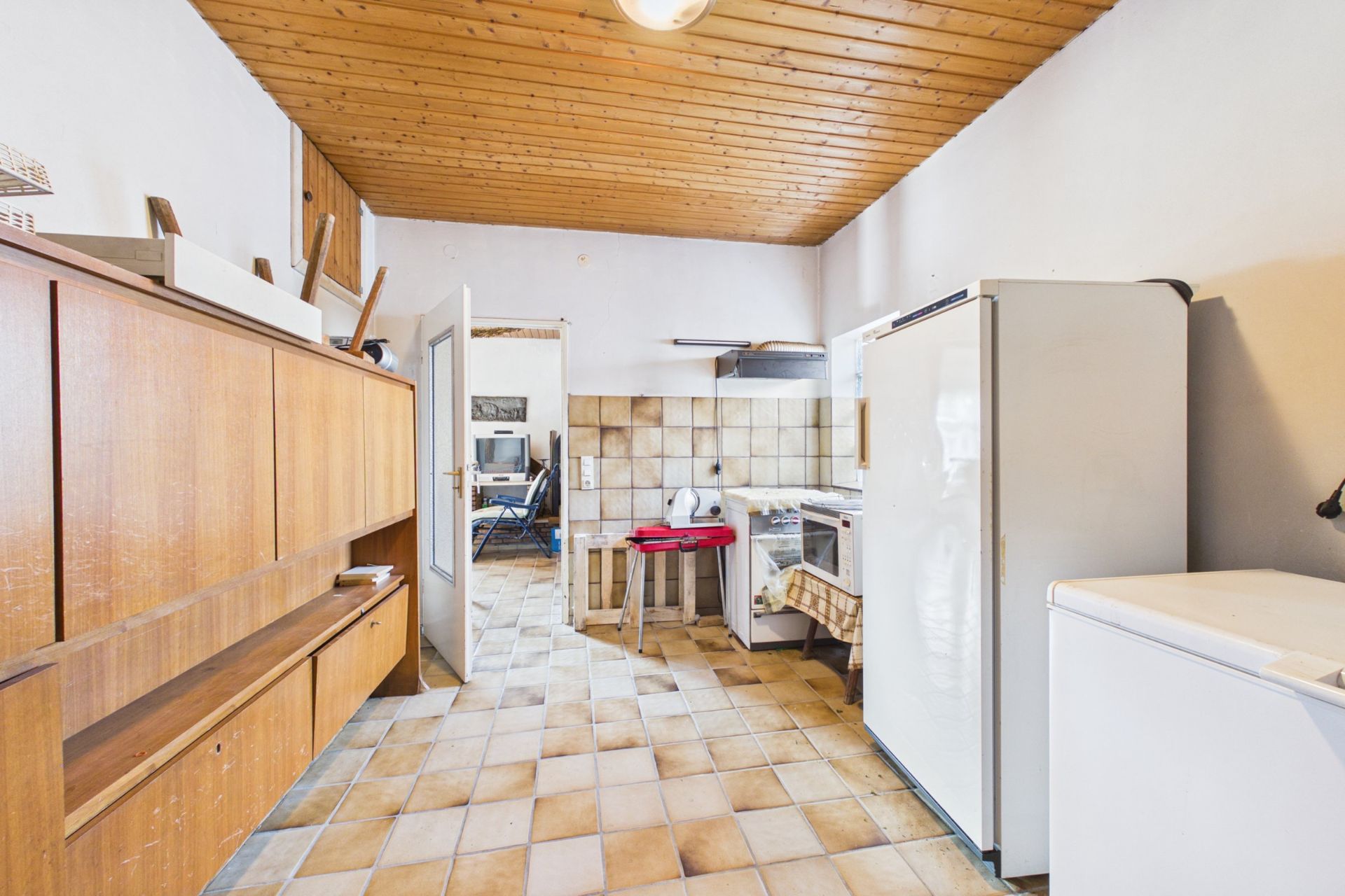 Küche mit Holzdecke, Fliesenboden, Kühlschrank, Gefrierschrank, Herd und Holzschrank.