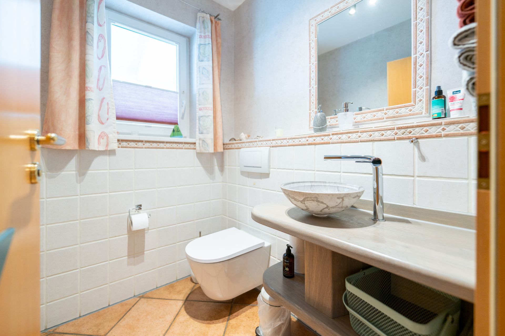 Helles Badezimmer mit Wandtoilette, rundem Waschbecken und großem Spiegel.