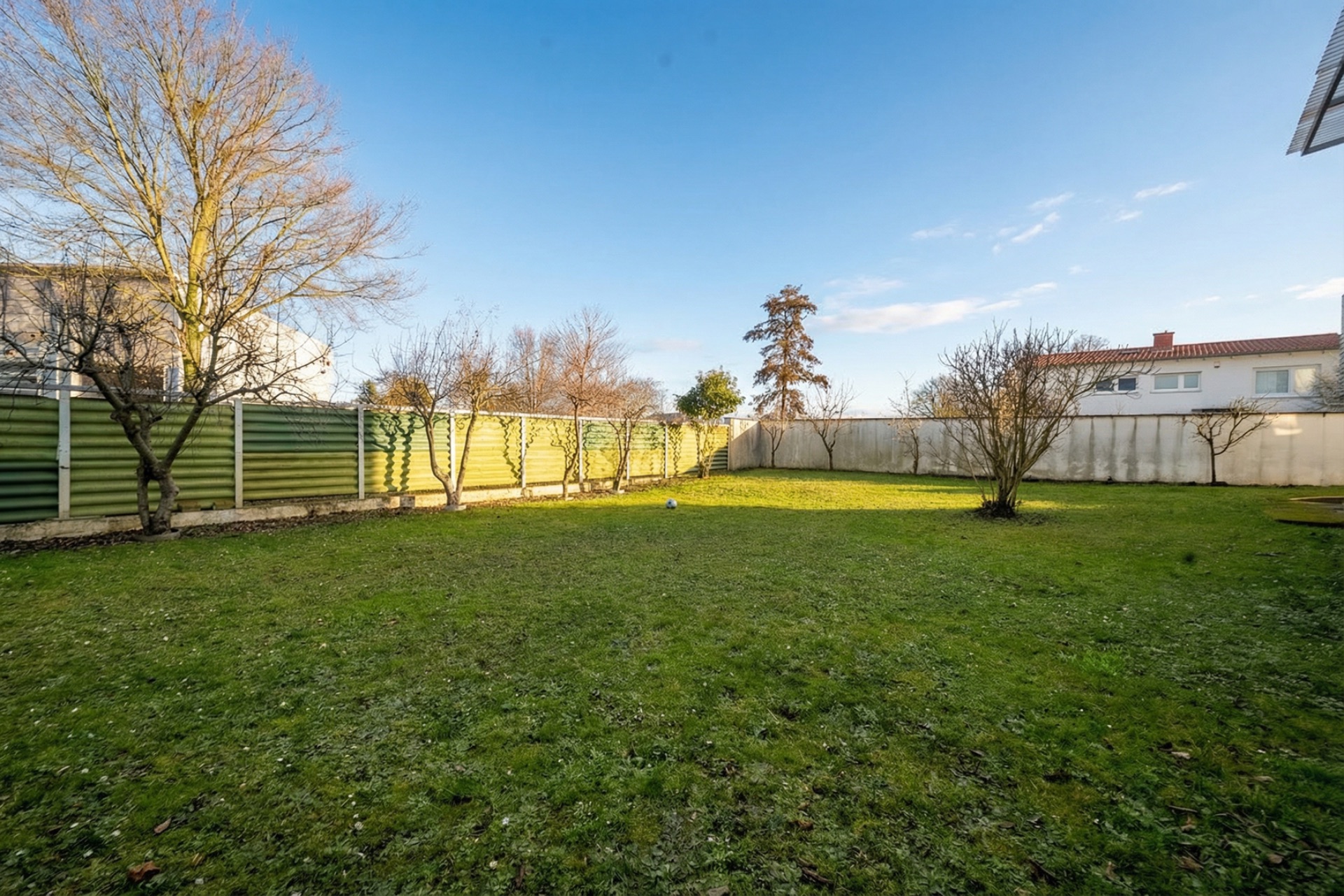 Großer grüner Garten mit Bäumen und Zaun bei klarem Himmel.