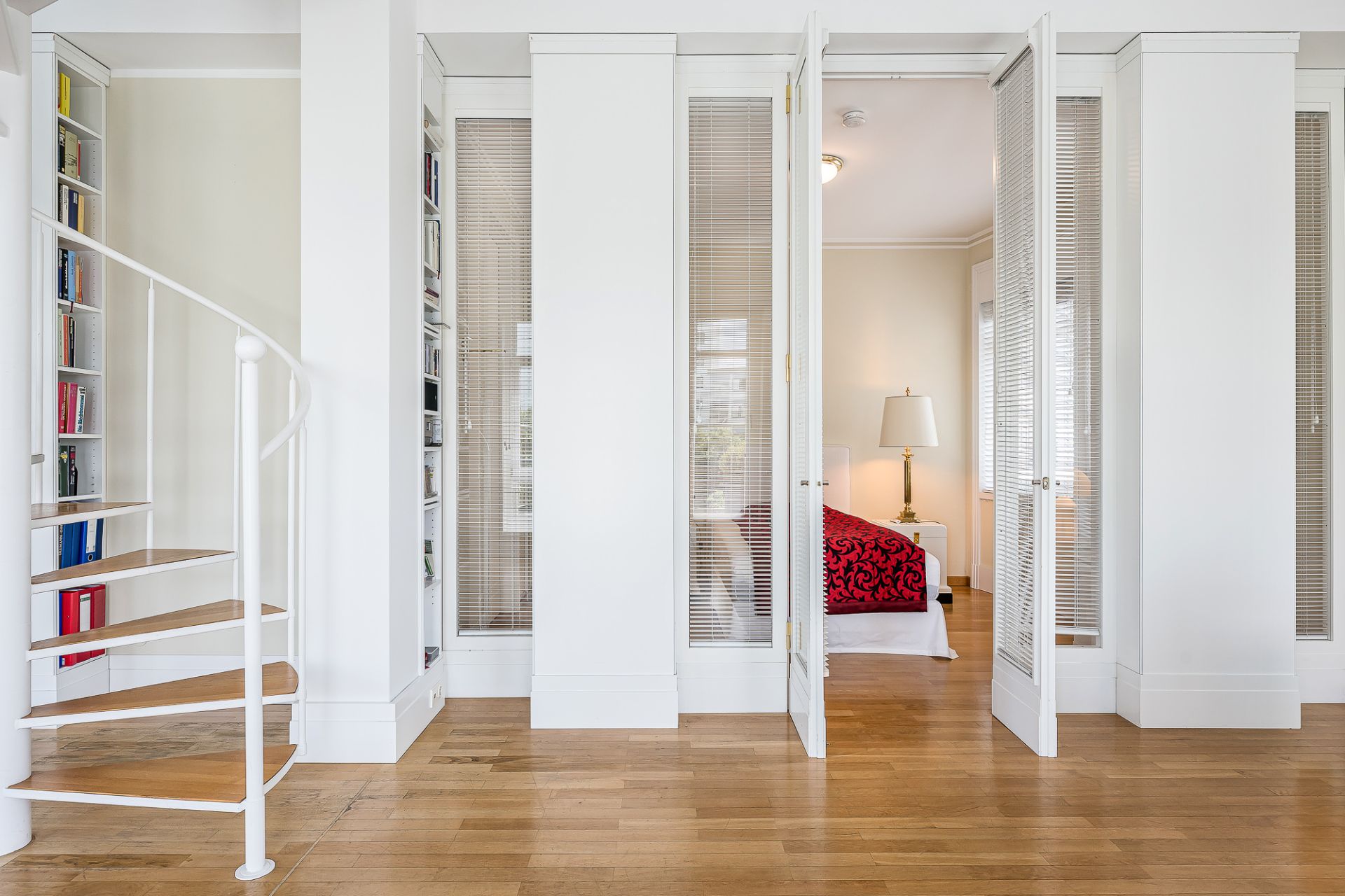 Heller Raum mit Holzfußboden, weißer Wendeltreppe und Glastüren zu einem Schlafzimmer.